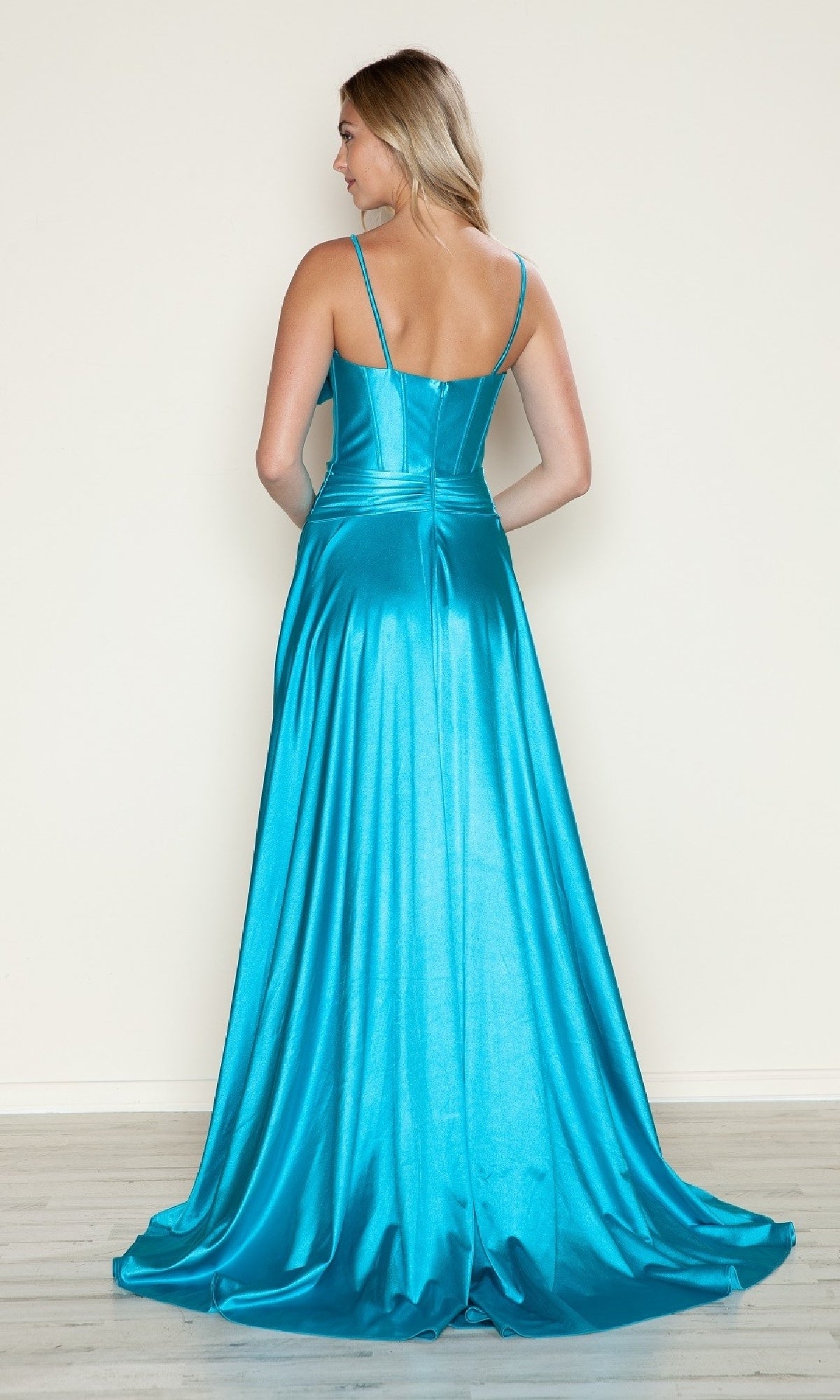 A woman faces away, wearing the Bow-Front Long Corset Prom Dress (Poly USA 9702)—a bright turquoise satin evening gown with thin straps and a flared skirt—against a plain, light-colored background.